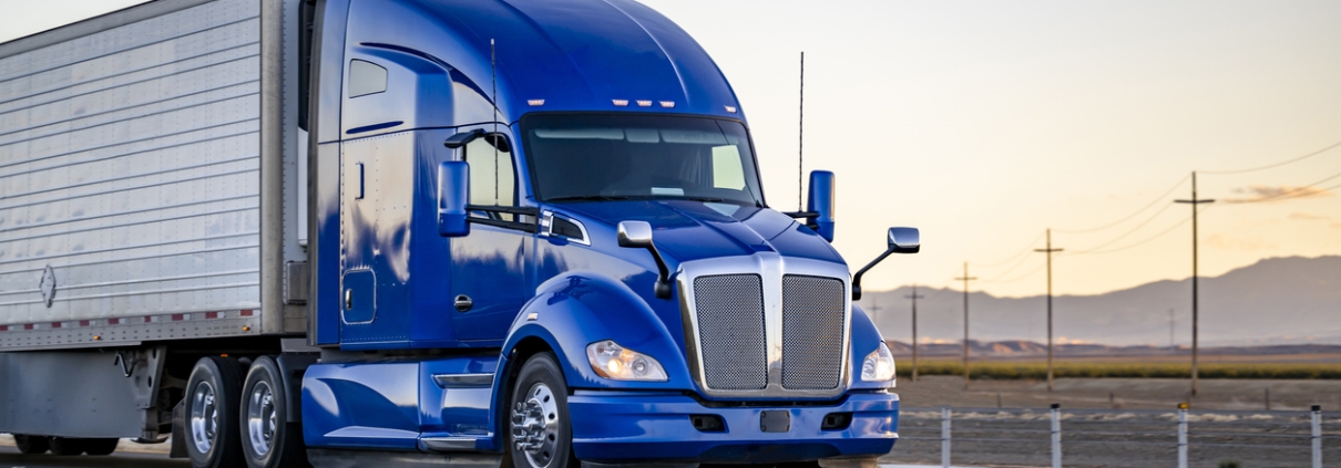 Industrial comfort big rig powerful blue semi truck tractor with high cab transporting frozen commercial cargo in refrigerator semi trailer running on the highway road at sunset in California