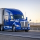Industrial comfort big rig powerful blue semi truck tractor with high cab transporting frozen commercial cargo in refrigerator semi trailer running on the highway road at sunset in California