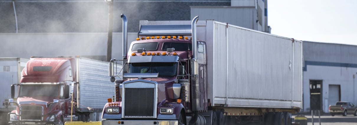 Pro commercial classic burgundy big rig semi truck tractor with chrome parts and container on semi trailer running on the road in industrial area raising a cloud of dust