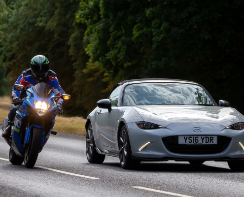 Man riding a Suzuki motorcycle overtakes a Mazda MX5 car on the A5