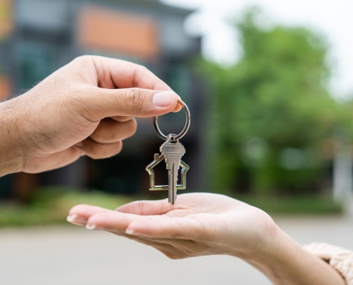 Woman buying or rent new home she holding key front of new house. Surprise happy young asian woman giving house key and smile to rent or purchase apartment home. Moving relocation concept.