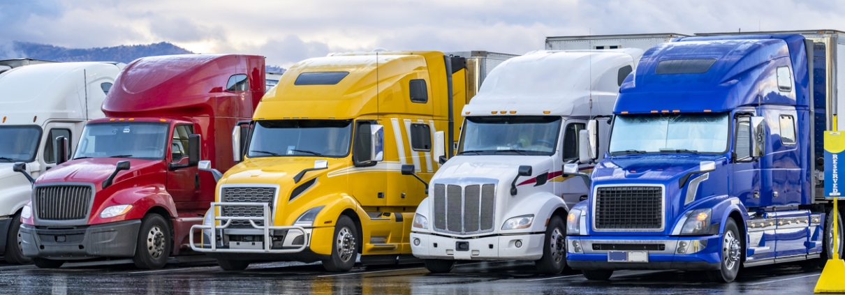 Industrial long hauler carriers big rig semi trucks with loaded semi trailers standing in row on truck stop parking lot for truck driver rest at early morning time according to the electronic logbook