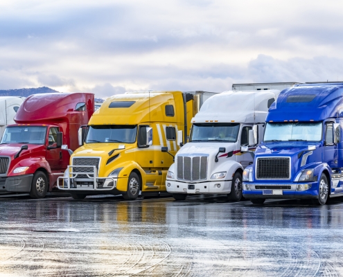 Industrial long hauler carriers big rig semi trucks with loaded semi trailers standing in row on truck stop parking lot for truck driver rest at early morning time according to the electronic logbook