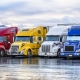 Industrial long hauler carriers big rig semi trucks with loaded semi trailers standing in row on truck stop parking lot for truck driver rest at early morning time according to the electronic logbook