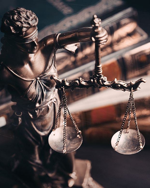 Bronze statue of lady justice holding a sword and scales, with a focused, dramatic lighting.