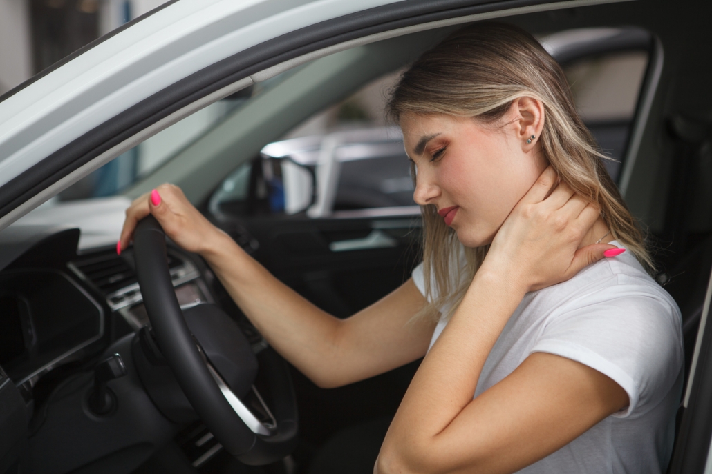 Young woman suffering from neck whiplash, sitting in drivers seat of her car