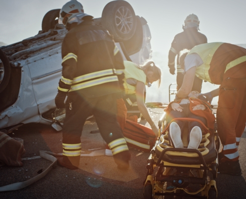 On the Car Crash Traffic Accident Scene: Rescue Team of Firefighters Pull Female Victim out of Rollover Vehicle, They Use Stretchers Carefully, Hand Her Over to Paramedics who Perform First Aid