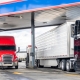 Industrial standard big rigs semi trucks with semi trailers standing on the fuel station parking lot filling the semi trucks tanks with diesel fuel to have ability continue commercial flight