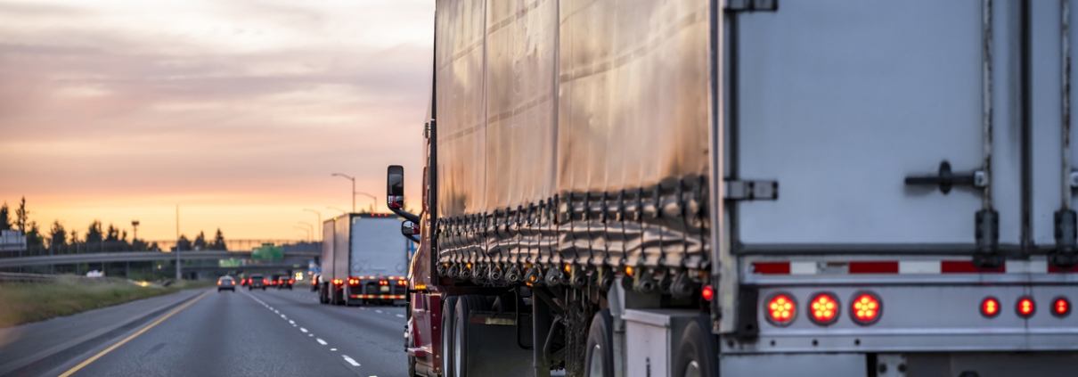 High cab long hauler freight burgundy big rig industrial semi truck tractor transporting commercial cargo in tented dry van semi trailer running on the highway road at twilight evening