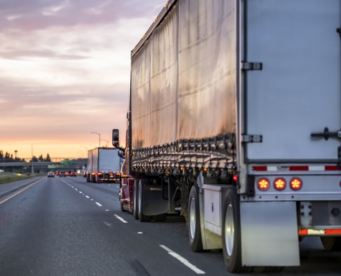 High cab long hauler freight burgundy big rig industrial semi truck tractor transporting commercial cargo in tented dry van semi trailer running on the highway road at twilight evening