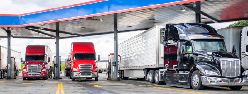 Long haulers big rigs semi trucks with semi trailers fuel tanks with diesel standing on the gas station on the truck stop