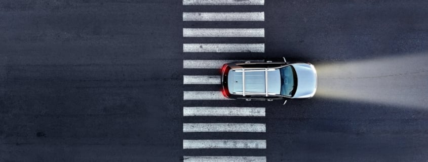 Aerial. A car with its headlights on drives over a pedestrian crosswalk at night. Top view from drone.