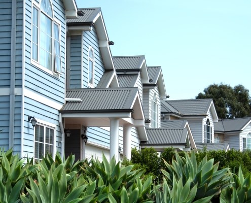 Frontal view of double-story townhouses characterized by their distinctive weatherboard wall cladding and corrugated metal roofs