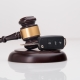 Close-up Of Gavel And Car Key On Sounding Block Against Grey Background