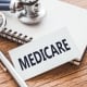 MEDICARE - text on card on wooden table with stethoscope and notepad for medical records.